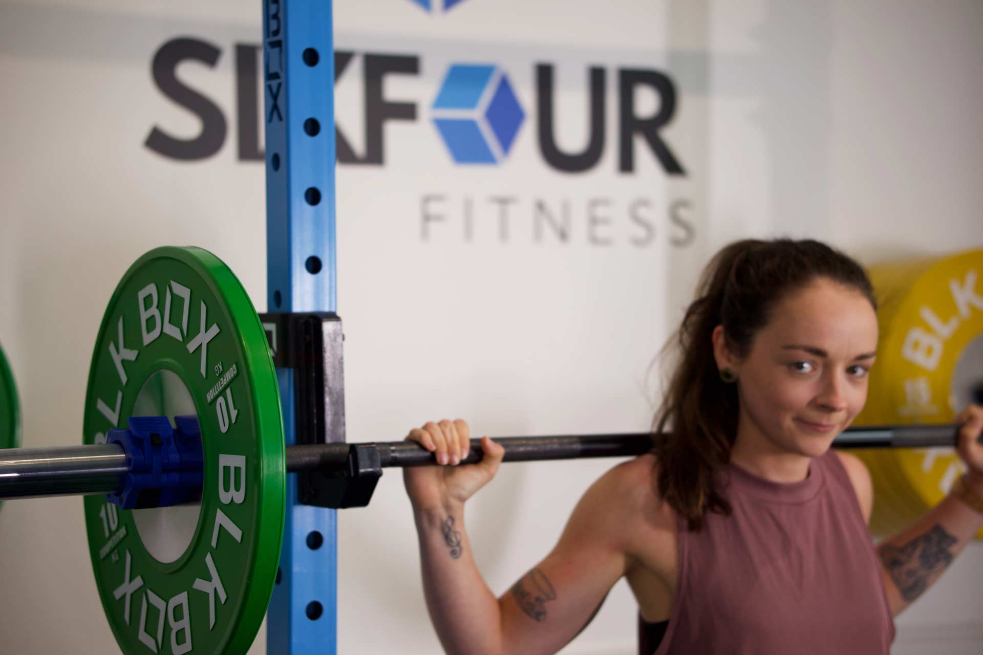 A woman lifting a barbell with a coach supervising at SixFour Fitness